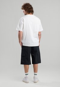 T-shirt en coton blanc, à manches courtes, coupe décontractée, associé à un short cargo sombre avec deux poches latérales et une coupe standard.