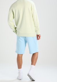 Sweat-shirt vert clair et short bleu clair avec une texture douce. Des chaussettes blanches aux chevilles et des baskets blanches complètent la tenue.