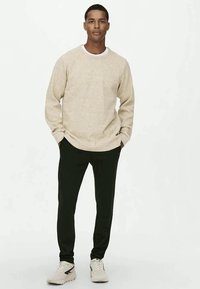 Beige textured sweatshirt with a round neckline and raglan sleeves, paired with black tapered pants and white athletic sneakers.