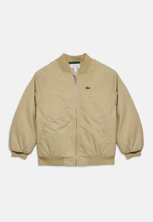 Beige zip-up bomber jacket with ribbed cuffs and hem, two front snap-button pockets, and a small green embroidered logo on the chest.