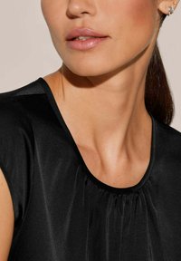 Schwarze Satinbluse mit kurzen Ärmeln, rundem Ausschnitt und plissiertem Detail am Kragen. Glatte Textur, elegantes Design.