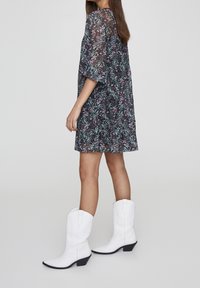 Květinové šaty v černé barvě s barevnými květinami, volný střih a krátké rukávy. V kombinaci s bílými kovbojskými botami na blokovém podpatku.