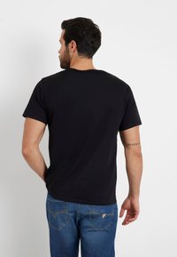 T-shirt nera in cotone con maniche corte, colletto rotondo e vestibilità comoda. Indossata con jeans blu con cuciture decorative sulle tasche.