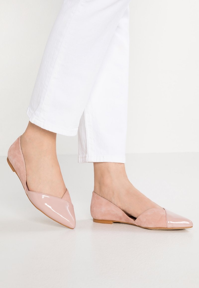 Ballerines roses à bout pointu avec un devant en cuir verni brillant et des côtés en suède mat. Elles présentent un talon bas et une coupe en V pour une silhouette élégante.