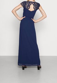 Abito blu navy con maniche in pizzo e dettagli sulla schiena, caratterizzato da un busto aderente e una gonna fluida. Chiusura a zip semplice sulla schiena.