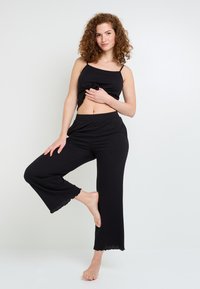 Completo loungewear a coste nere composto da un top corto con spalline sottili e pantaloni a gamba larga con orli sfilacciati, realizzato in tessuto morbido.