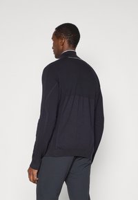 Sweater de malha azul-marinho com colarinho alto, design texturizado e acabamento mais claro em contraste ao longo da parte de trás do yoke e ombros. Mangas longas.