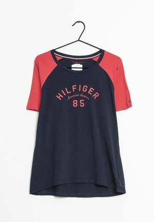 Camicia a maniche corte blu navy e rossa con la scritta "HILFIGER 85 American dreamer", appesa a una gruccia nera su sfondo bianco.