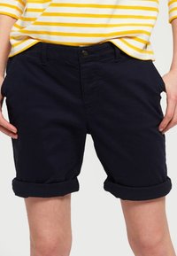 Navy cotton shorts with cuffed hems, featuring a front button closure and pockets on both sides. Suitable for casual wear.