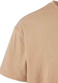 Beige T-shirt met korte mouwen van zachte katoenen stof. Beschikt over een ronde halslijn en minimale stikseldetails, met een gladde textuur.