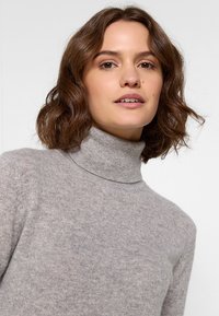 Hellgrauer Rollkragenpullover aus weichem, strukturiertem Material. Besitzt ein tailliertes Design und einen gerippten Kragen, ideal für legere Anlässe.
