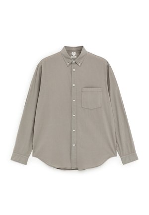 Beige Hemd mit langen Ärmeln, Knopfleiste, einer Brusttasche und Knopfleiste am Kragen, flach auf weißem Hintergrund liegend.