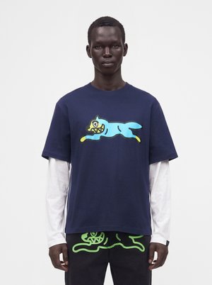 Man wearing layered white long sleeves under a navy blue T-shirt with a blue cartoon dog and black pants with a green cartoon design.