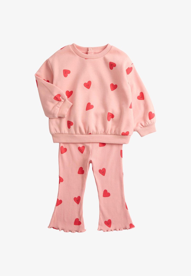 Sudadera rosa con estampados de corazones rojos, puños y cinturilla elásticos. Pantalones acampanados a juego en rosa con estampados dispersos de corazones rojos.