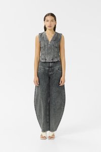 Femme portant un gilet sans manches en denim noir délavé et un pantalon large assorti en denim noir délavé avec des talons ouverts blancs.