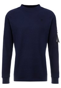 Mörkblå långärmad skjorta i texturerad tyg, med hög krage och en ficka med dragkedja på vänster ärm.