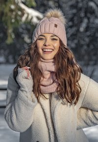 Beanie rosa lavorato a maglia con pom-pom in pelliccia, abbinato a una sciarpa rosa coordinata e un cappotto bianco soffice. Mostra un accogliente outfit invernale.