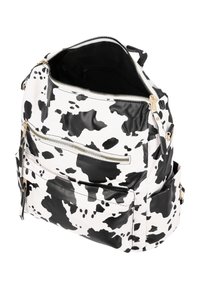 Zaino in stampa mucca bianco e nero con hardware dorato, scompartimenti con zip e finitura in pelle testurizzata. La parte superiore aperta rivela un interno nero.