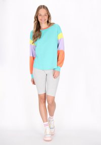 Maglietta turchese a maniche lunghe con maniche a righe multicolori, abbinata a pantaloni corti grigi. Presenta una vestibilità comoda e un tessuto morbido.