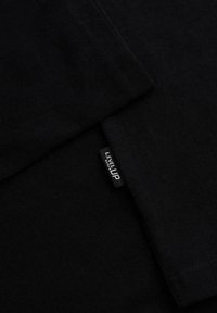 Tissu noir avec coutures visibles et petite étiquette noire marquée « LEVEL UP » cousue dans la couture.