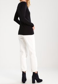 Schwarzes Langarmoberteil, kombiniert mit weißen Hosen mit umgeschlagenen Ärmeln und schwarzen Wildleder-Stiefeletten, die ein figurnahes Design und eine glatte Textur zeigen.