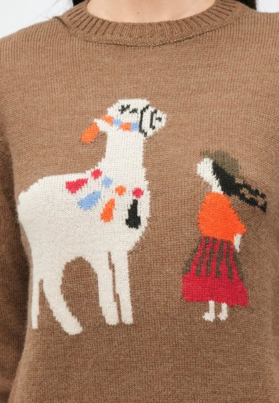 Pruun kampsun, millel on valge llama ja naise kudumismuster, kes kannab punast seelikut ja rohelist kübarat ning on teineteise poole suunatud.