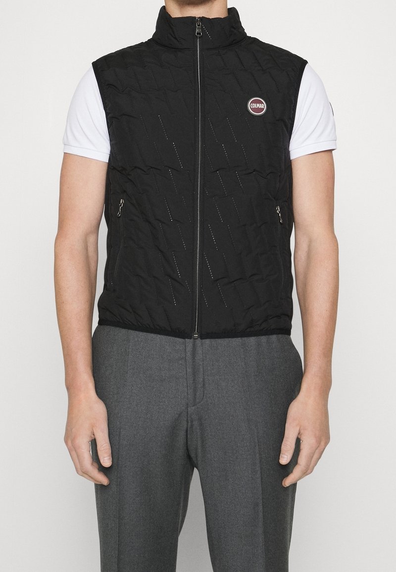 Veste sans manches noire matelassée avec un col montant, dotée d'une fermeture éclair frontale et de motifs de coutures diagonales. Comprend des poches latérales.