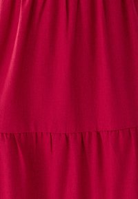 Tela de vestido fucsia con textura suave, con un diseño fruncido y estratificado en el dobladillo. La superficie es lisa, sin patrones ni adornos.