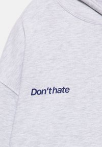Felpa grigia con una texture morbida e una vestibilità comoda, con la scritta "Don't hate" ricamata in blu navy nella zona del petto.