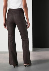 Pantaloni flared, de culoare maro, care se mulează pe corp, cu o textură netedă și două buzunare pe spate. Stilizați cu un talie înaltă și detalii discrete de coasere.