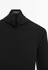 Maglione a collo alto a maglia nera con maniche lunghe. Realizzato in tessuto morbido, presenta cuciture minime e un'etichetta all'interno.