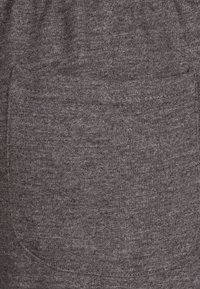 Tejido gris de un par de pantalones con un tejido texturizado, con un detalle de bolsillo aplicado en el lateral para almacenamiento.