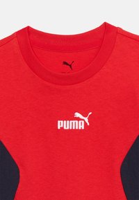 Κόκκινο μπλουζάκι Puma με στρογγυλή λαιμόκοψη, λευκό λ ογότυπο Puma και μαύρες πλευρικές λωρίδες ορατές μόνο στην περιοχή του κορμού.