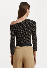Svart off-shoulder topp med lange ermer, prydet med et mønster av små beige prikker; kombinert med høyt liv beige bukser og et flettet svart belte.