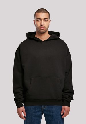 Svart hettegenser laget av myk stoff, med en frontlomme og ribbestrikkede mansjetter. Kombinert med blå jeans. Enkelt design, uten mønstre.