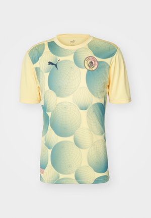 Jersey de Puma del Manchester City en amarillo claro con patrones de círculos azules superpuestos. Cuenta con cuello redondo y el logo del equipo en el pecho.