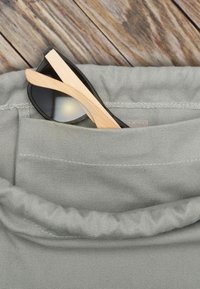 Una tasca di tessuto grigio con occhiali da sole incorniciati in bambù, con lenti scure e bracci in legno chiaro visibili contro il materiale testurizzato.