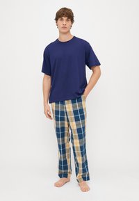 Jūros laivyno marškiniai su apvalia apykakle, derinami su languotais pižamos džinsais mėlynos, geltonos ir pilkos spalvų. Kelnės turi laisvą kirpimą ir tiesių kojų dizainą.