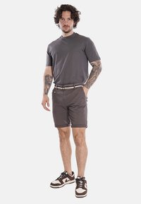 T-shirt grigia in cotone abbinata a pantaloni corti grigi scuri, con una cintura a righe multicolori e sneaker marroni con dettagli crema.