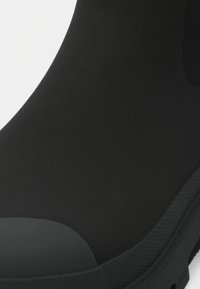 Botte de cheville en caoutchouc noire avec une finition mate lisse, un bout rond, une semelle texturée et un design sans coutures pour minimiser l'intrusion d'eau.