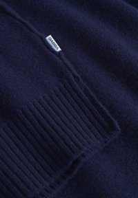 Mörkbl�å stickad tröja med ribbade ärmslut, mjuk textur och en liten tygetikett med texten "GABBA" sydd nära sömmen.