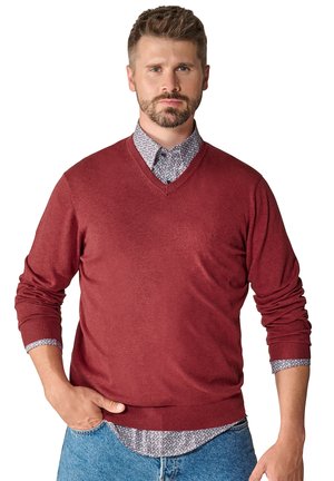 Czerwony sweter w serek wykonany z gładkiej dzianiny, z prążkowanymi mankietami i dołem. Noszony na wzorzystą koszulę, o luźnym kroju.