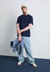 Námořnické bavlněné tričko s malým logem, světle modré oversized džíny a bílé tenisky s červenými akcenty. Světle zbarvená kšiltovka a bunda.
