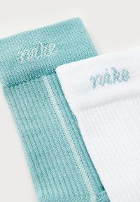 Nike čarape u tirkiznoj i bijeloj boji, s rebrastom teksturom i izvezenim logotipom. Tirkizna čarapa ima jednoličnu boju, dok je bijela s naglaskom u tirkiznoj.