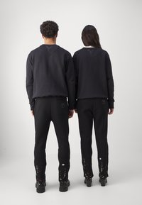 Svart hettegenser og bukser med teksturert stoff. Buksene har et fargerikt sprutmønster på kanten. Begge har et enkelt design og passform.