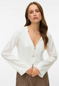 Hvid bluse med lange ærmer, V-hals og tre sølvfarvede knapper. Glat stof med en struktureret pasform og let udvidede ærmer.