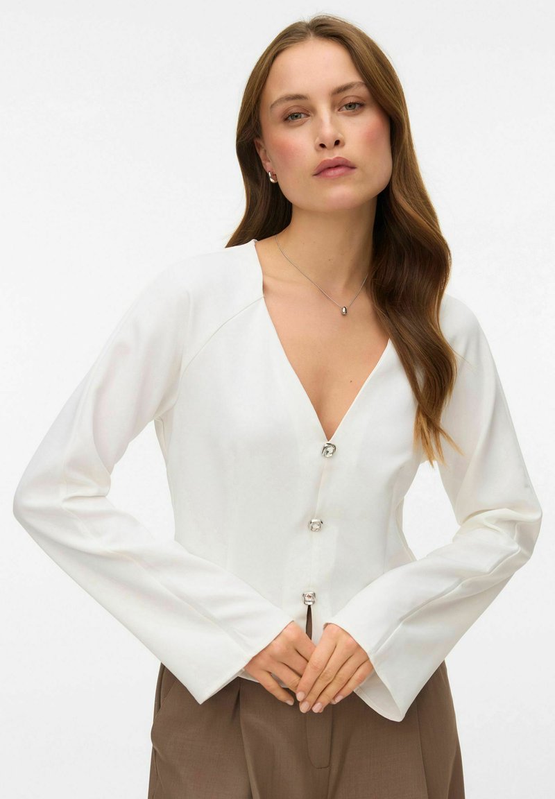 Hvid bluse med lange ærmer, V-hals og tre sølvfarvede knapper. Glat stof med en struktureret pasform og let udvidede ærmer.