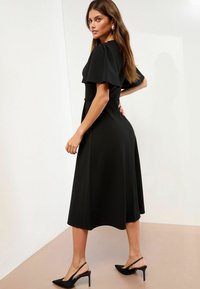 Rochie midi neagră cu mâneci scurte tip flutură, bust ajustat și fustă evazată. Purtați-o cu pantofi slingback cu toc negru.