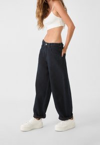 Tummansiniset, leveälahkeiset farkut, joissa on korkea vyötärö, etutaskut ja käännetyt lahkeet, yhdistettynä valkoisiin tennareihin.