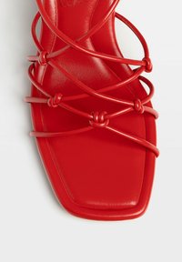 Sandale plate rouge avec un design à bout carré, dessus en cuir lisse et bandes entrecroisées décoratives avec des nœuds ronds.